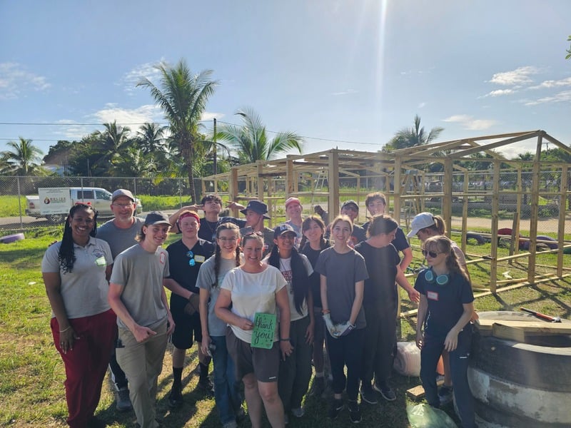 A team and local leader celebrating at a construction site with a thank-you sign