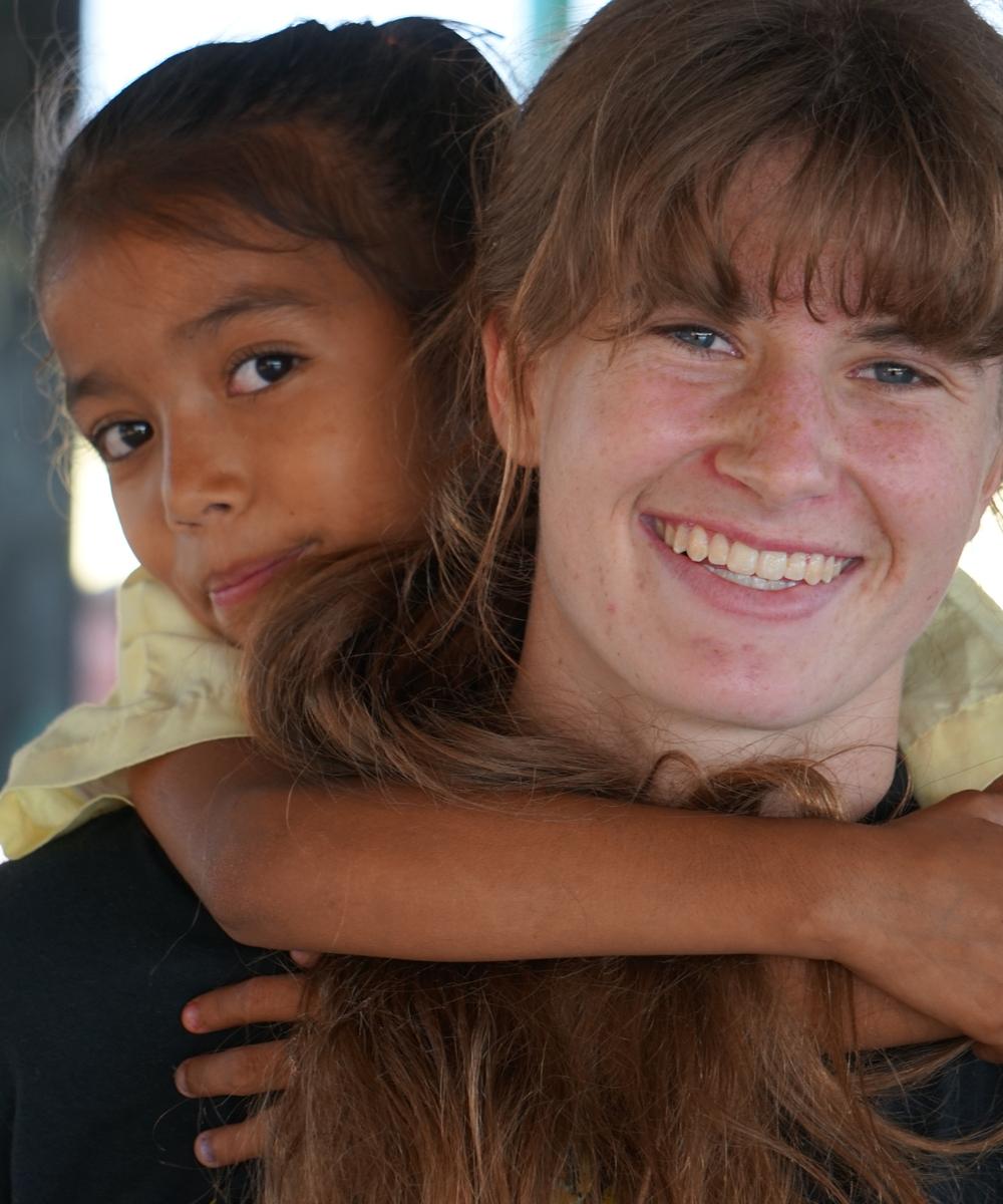 A smiling volunteer being hugged from behind by a child