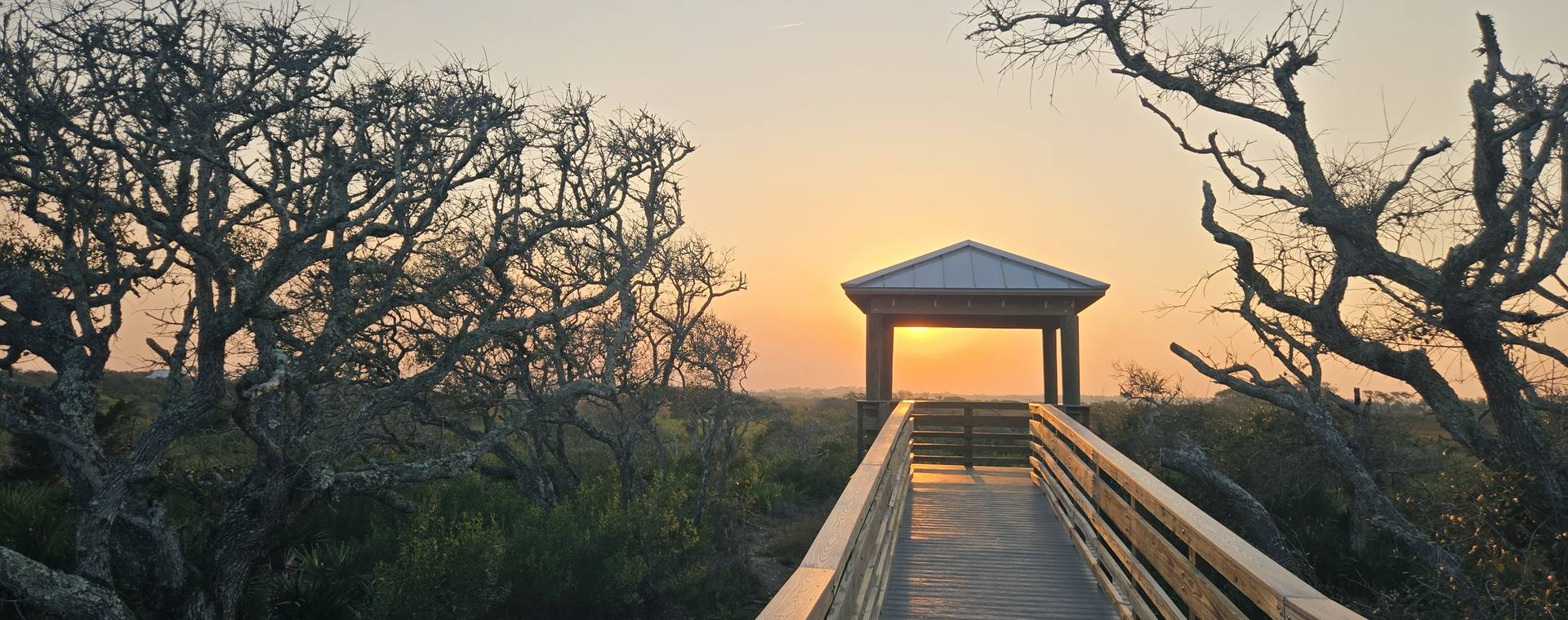A wooden boardwalk leading to a gazebo at sunset