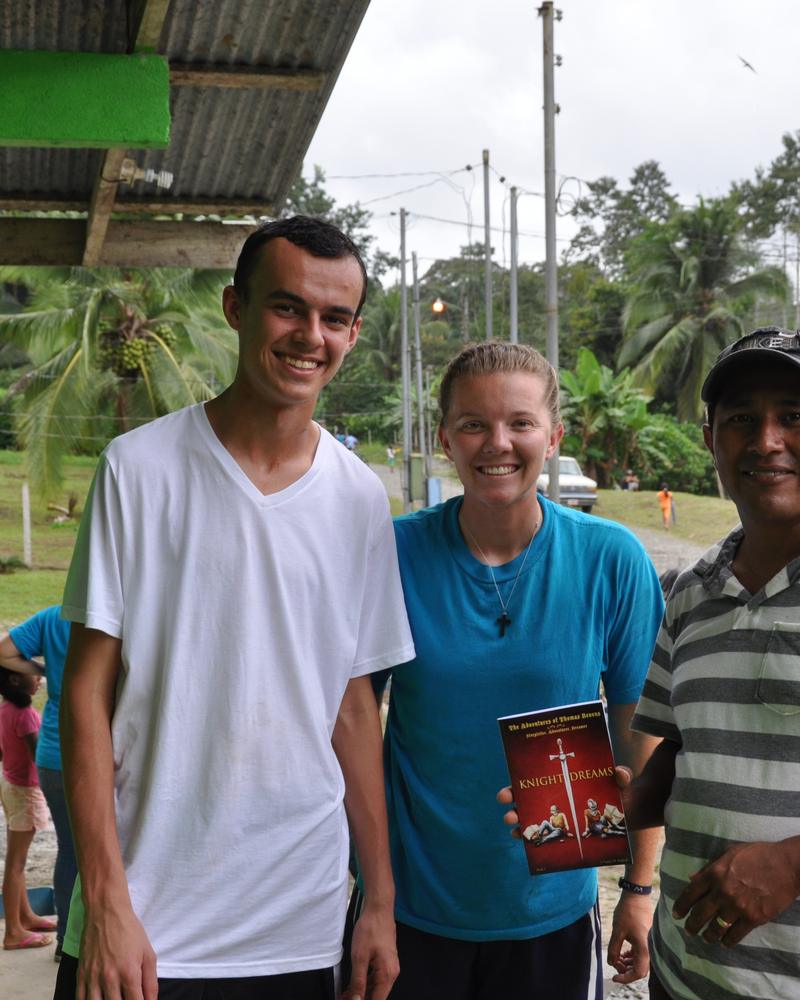 Two smiling volunteers and a local ministry leader standing together in a village