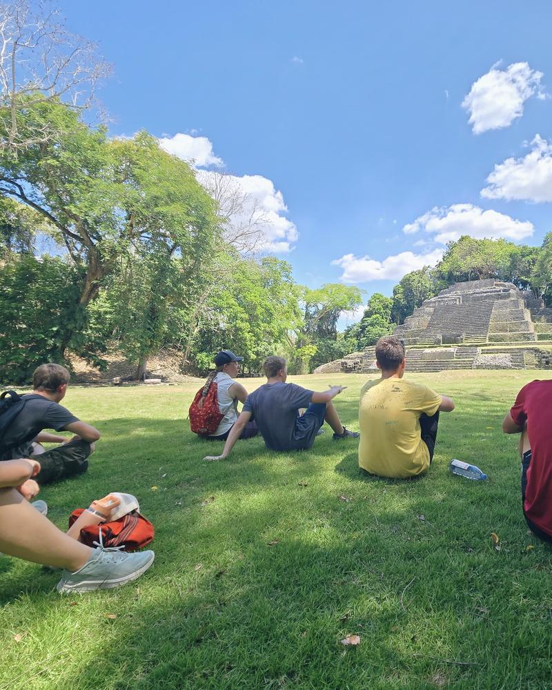 Students resting on the grass in front of an ancient Maya temple in Belize