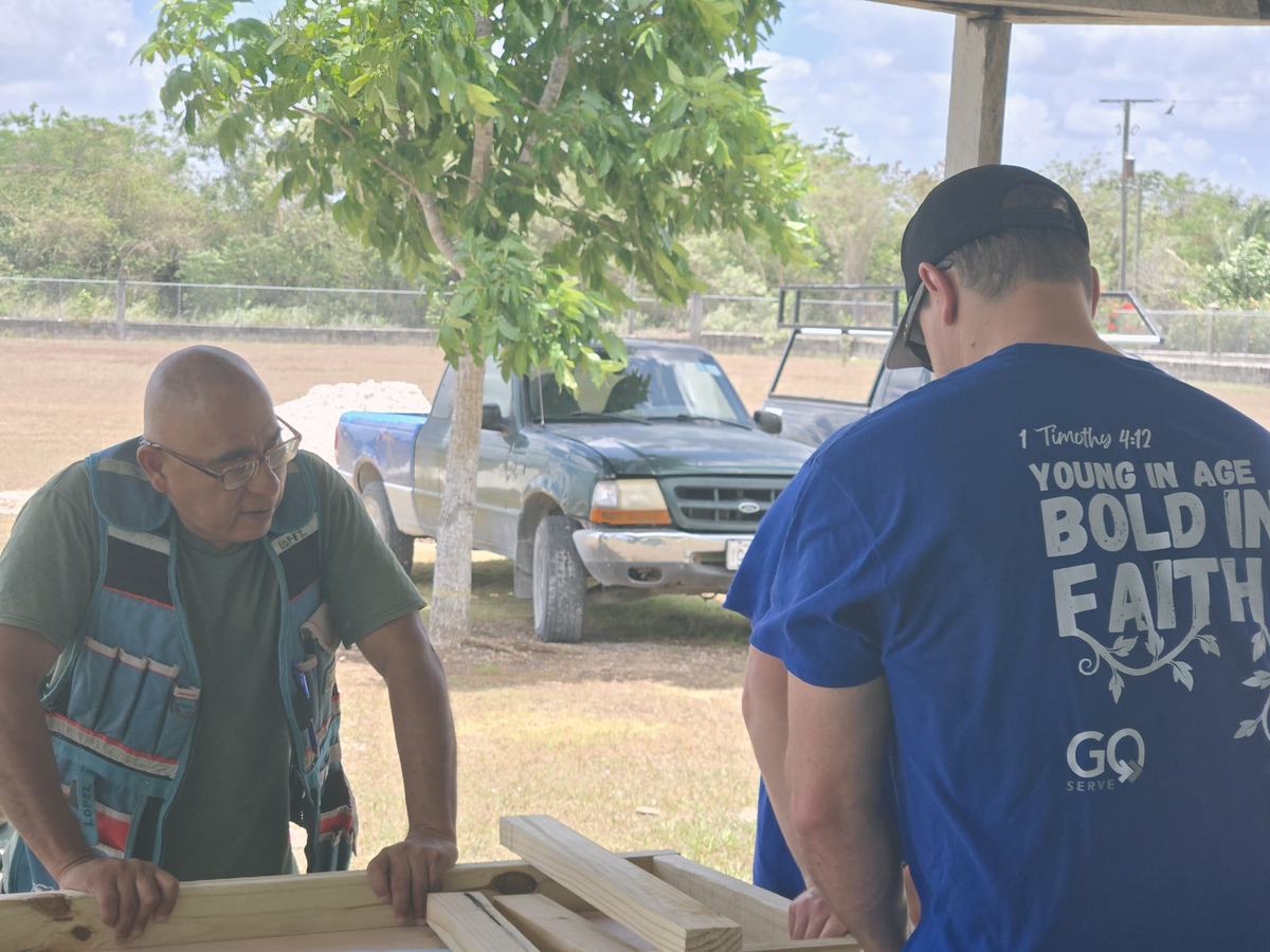 A GO Serve volunteer and a local carpenter working together on a wooden frame